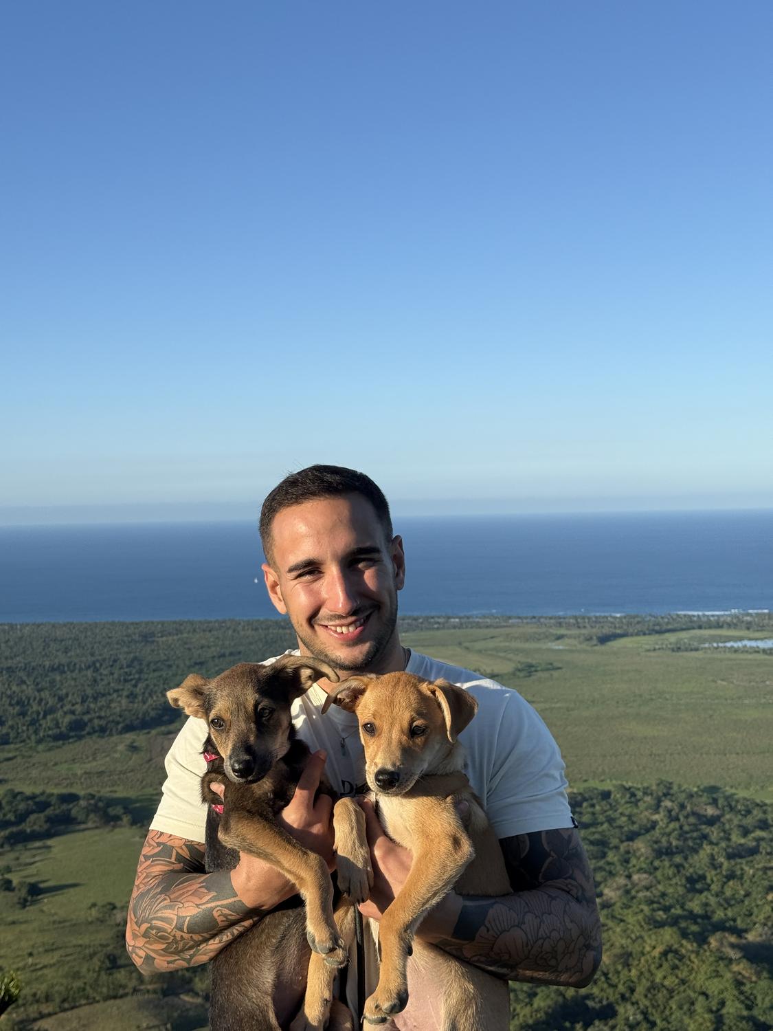 Adrián con dos cachorros en brazos y el mar de fondo